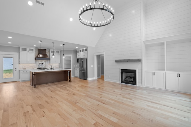 kitchen with hanging light fixtures, stainless steel refrigerator with ice dispenser, a center island with sink, white cabinets, and high vaulted ceiling