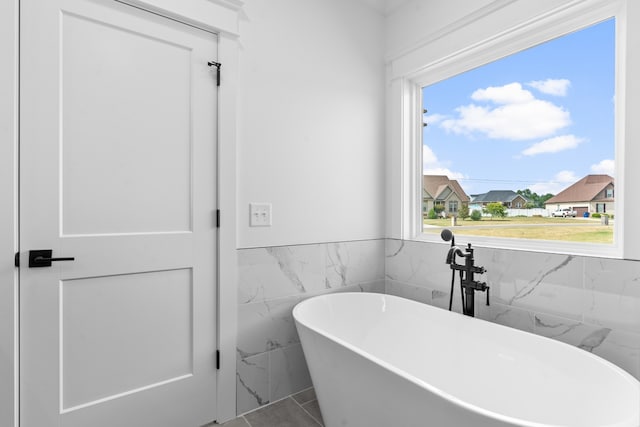 bathroom with tile walls, a washtub, and tile patterned flooring