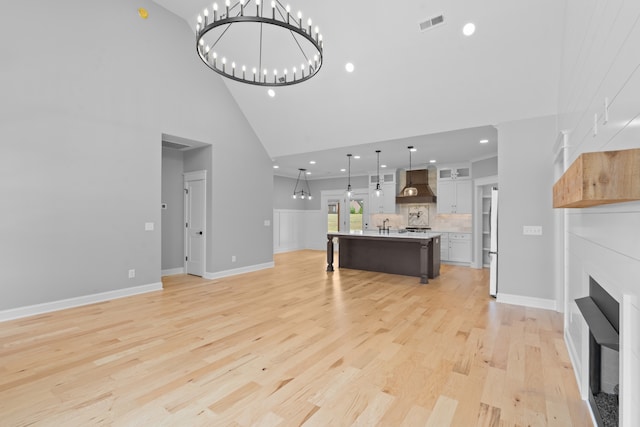 unfurnished living room with light hardwood / wood-style flooring, a chandelier, and high vaulted ceiling