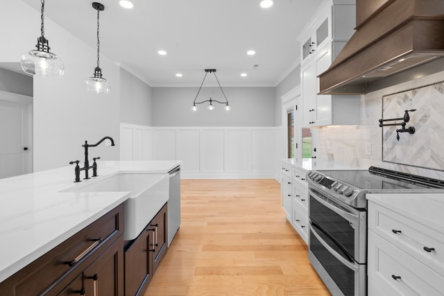 kitchen with stainless steel appliances, white cabinets, decorative light fixtures, light wood-type flooring, and premium range hood