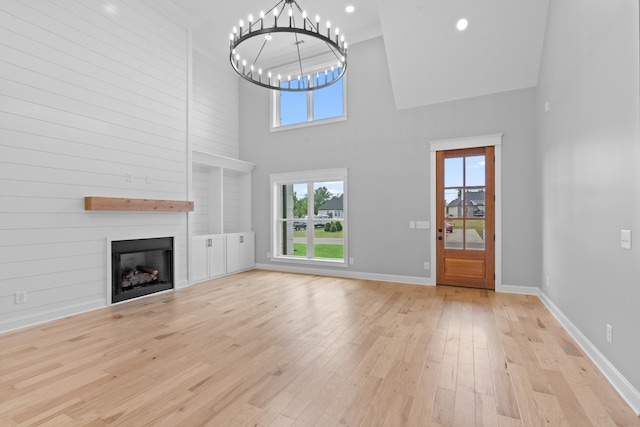 unfurnished living room with a high ceiling, light hardwood / wood-style flooring, a fireplace, and an inviting chandelier