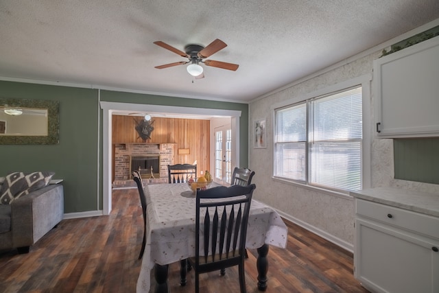 dining area featuring a textured ceiling, dark hardwood / wood-style flooring, a brick fireplace, ceiling fan, and ornamental molding