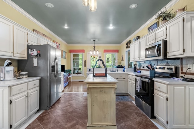 kitchen with white cabinets, hanging light fixtures, appliances with stainless steel finishes, a kitchen island with sink, and crown molding