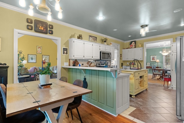 kitchen featuring stainless steel appliances, ornamental molding, decorative light fixtures, an inviting chandelier, and white cabinets