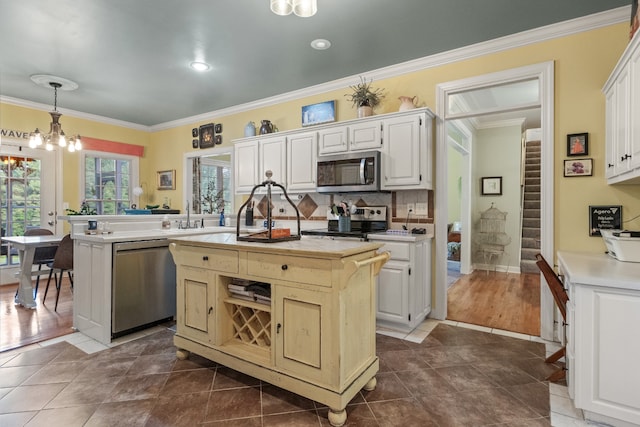 kitchen featuring hanging light fixtures, appliances with stainless steel finishes, an inviting chandelier, a kitchen island with sink, and crown molding