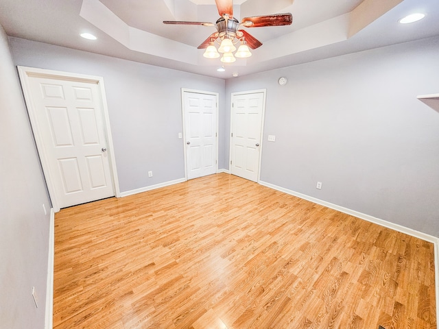 spare room with light hardwood / wood-style floors, a raised ceiling, and ceiling fan