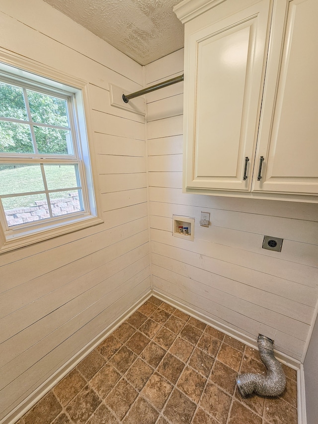 laundry room with hookup for an electric dryer, a textured ceiling, cabinets, and wood walls