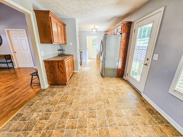 kitchen with a textured ceiling, stainless steel refrigerator, and light hardwood / wood-style flooring