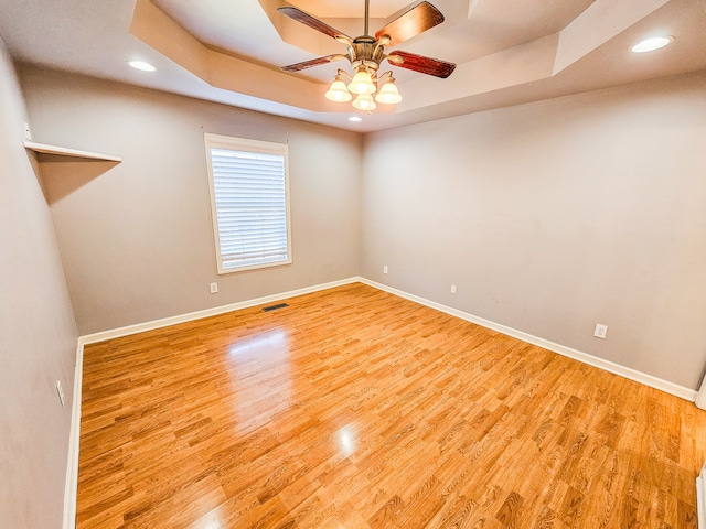 empty room with light hardwood / wood-style floors, a raised ceiling, and ceiling fan