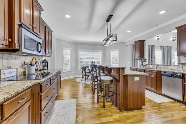 kitchen with light hardwood / wood-style flooring, crown molding, sink, decorative light fixtures, and appliances with stainless steel finishes