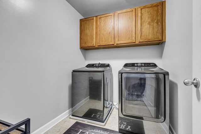 clothes washing area with washing machine and dryer, light tile patterned floors, and cabinets