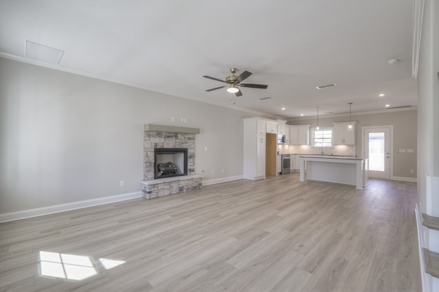 unfurnished living room featuring light hardwood / wood-style floors, a stone fireplace, crown molding, and ceiling fan