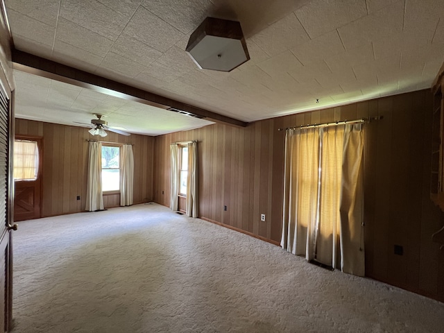 carpeted empty room with ceiling fan, beam ceiling, and wooden walls