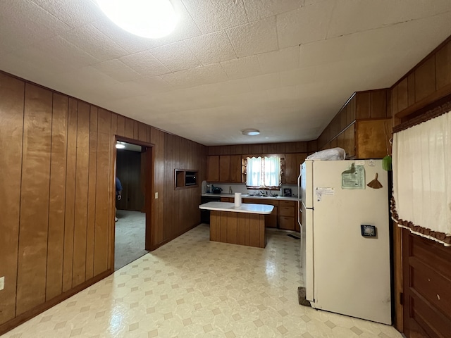 kitchen with wooden walls, a kitchen island, sink, and white refrigerator