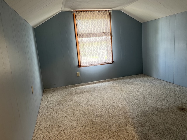 additional living space featuring carpet, vaulted ceiling, and wood walls