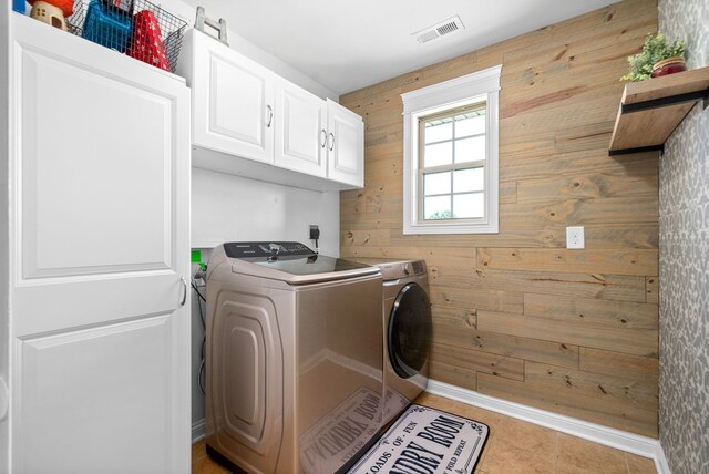 laundry area with cabinets, light tile patterned flooring, wooden walls, and washing machine and dryer