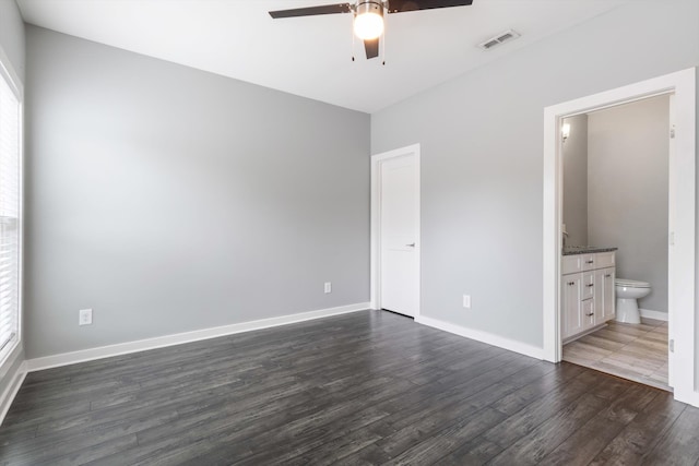 unfurnished bedroom with multiple windows, dark hardwood / wood-style floors, connected bathroom, and ceiling fan