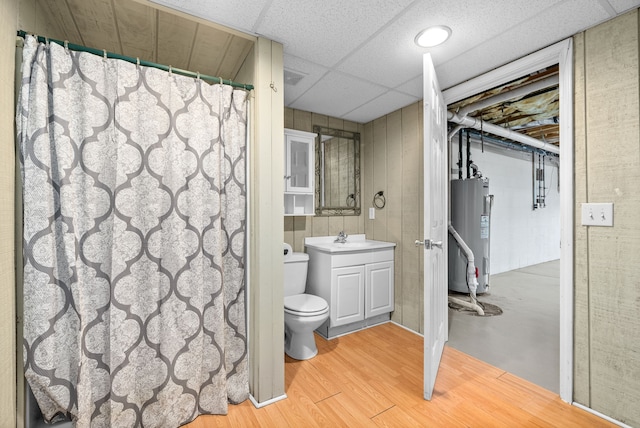 bathroom with a drop ceiling, toilet, vanity, hardwood / wood-style flooring, and electric water heater