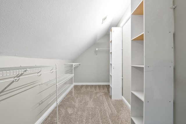 walk in closet with vaulted ceiling and light carpet