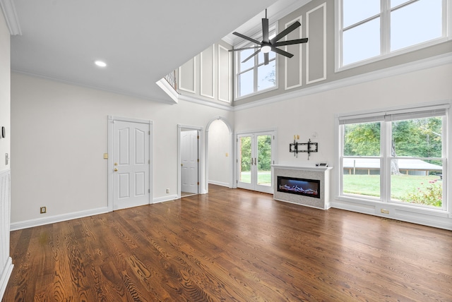 unfurnished living room with dark wood-type flooring, ceiling fan, a towering ceiling, and ornamental molding