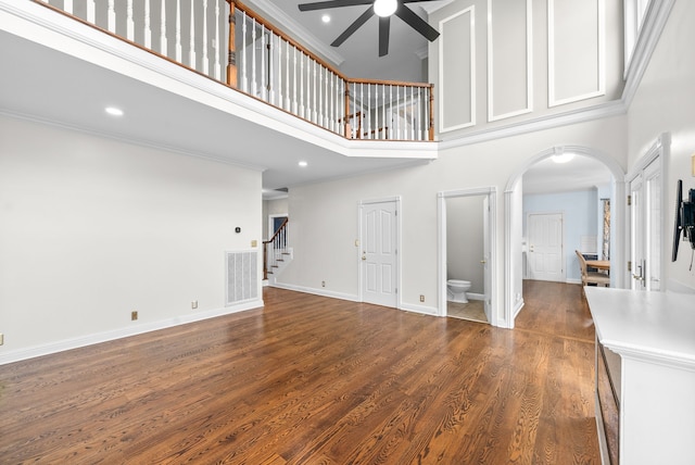 unfurnished living room with a towering ceiling, ornamental molding, dark wood-type flooring, and ceiling fan