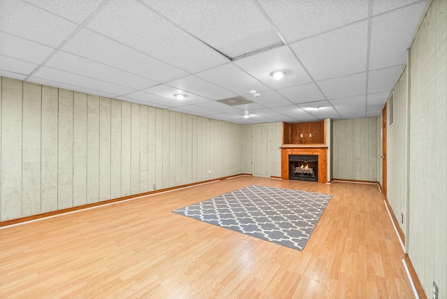 basement with a paneled ceiling, light hardwood / wood-style flooring, and wooden walls