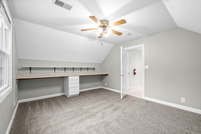 unfurnished office featuring built in desk, light carpet, vaulted ceiling, and ceiling fan