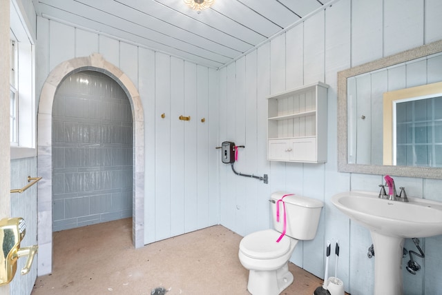 bathroom featuring toilet, sink, wooden walls, and concrete floors