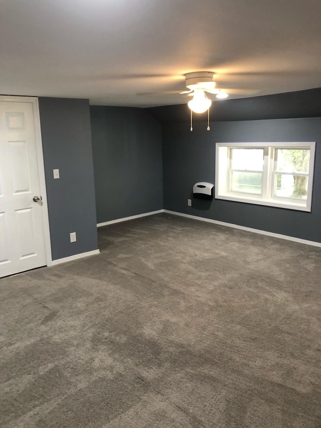 empty room featuring dark colored carpet, a ceiling fan, and baseboards