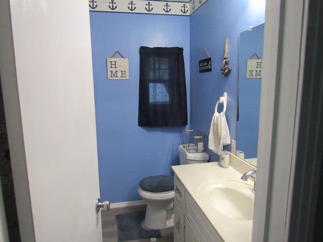 half bathroom featuring toilet, baseboards, and vanity