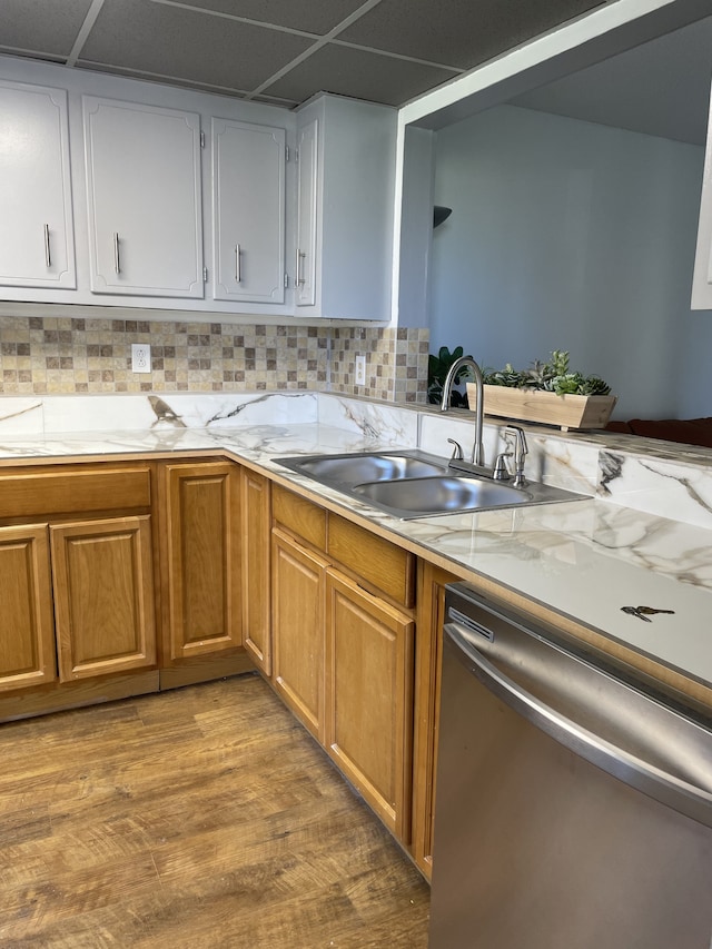 kitchen with sink, a drop ceiling, stainless steel dishwasher, decorative backsplash, and light hardwood / wood-style flooring