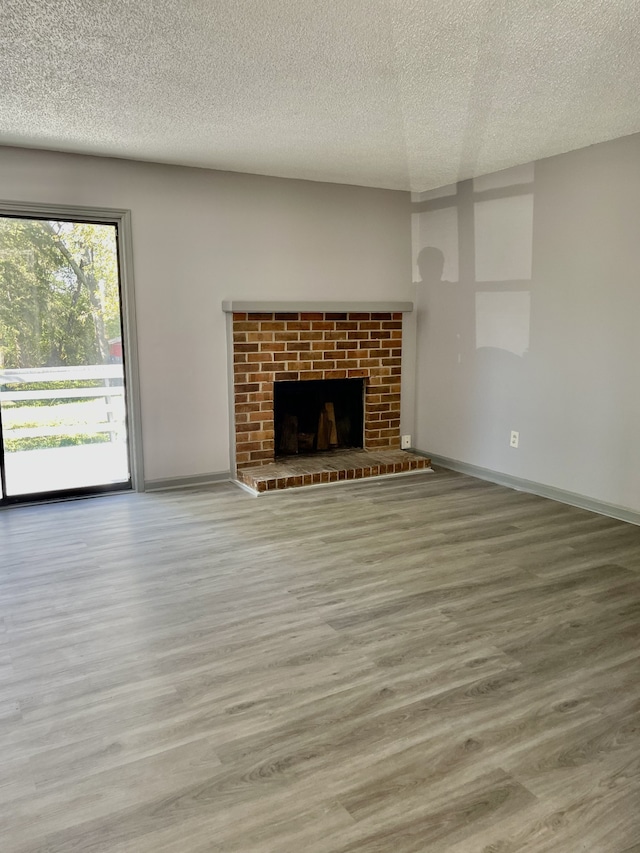 unfurnished living room featuring hardwood / wood-style flooring, a textured ceiling, and a brick fireplace