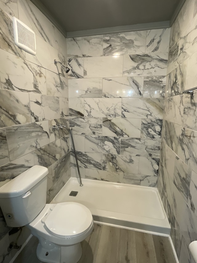 bathroom featuring a tile shower, hardwood / wood-style flooring, tile walls, toilet, and crown molding