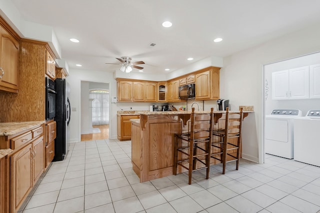 kitchen featuring kitchen peninsula, ceiling fan, a kitchen bar, separate washer and dryer, and black appliances