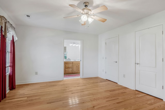 unfurnished bedroom with multiple closets, ensuite bath, light wood-type flooring, and ceiling fan