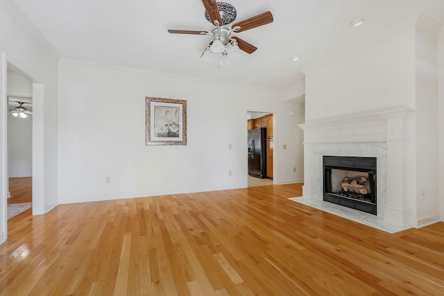 unfurnished living room featuring ornamental molding, a tiled fireplace, light wood-type flooring, and ceiling fan