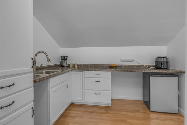 kitchen featuring lofted ceiling, white cabinets, sink, stainless steel fridge, and light hardwood / wood-style floors