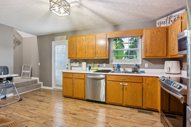 kitchen with sink, appliances with stainless steel finishes, a textured ceiling, and light hardwood / wood-style floors