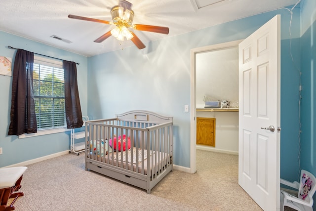 carpeted bedroom with a crib and ceiling fan