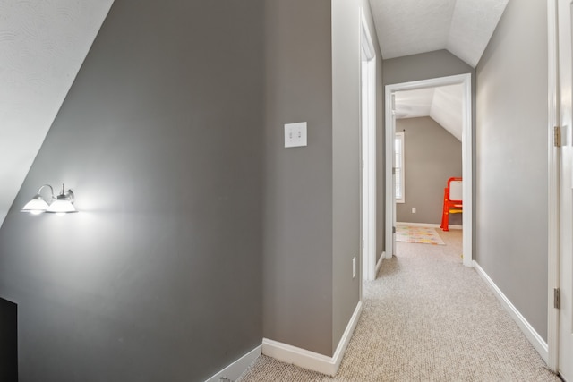 hallway featuring lofted ceiling, a textured ceiling, and light colored carpet