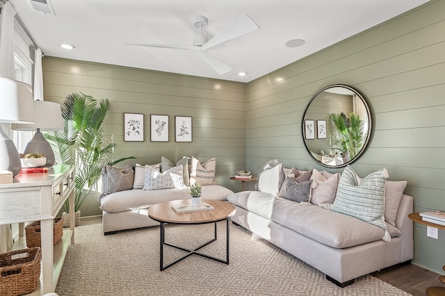 living room with wooden walls, wood-type flooring, and ceiling fan