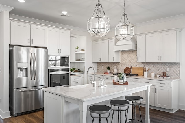 kitchen featuring white cabinets, decorative light fixtures, stainless steel appliances, and an island with sink