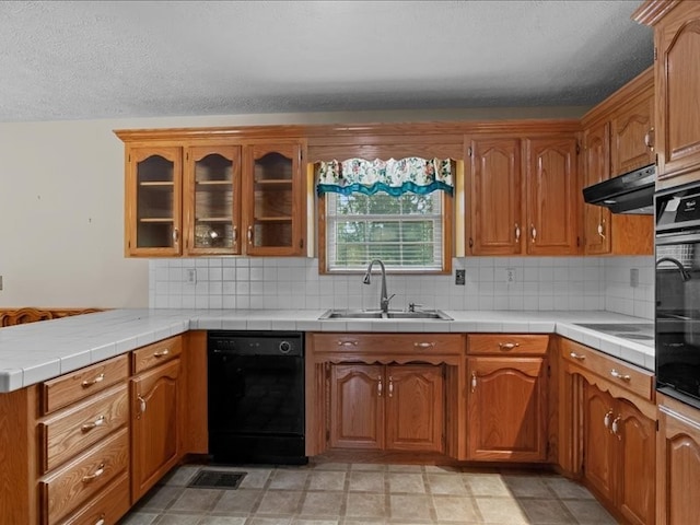 kitchen with kitchen peninsula, decorative backsplash, black appliances, tile counters, and sink