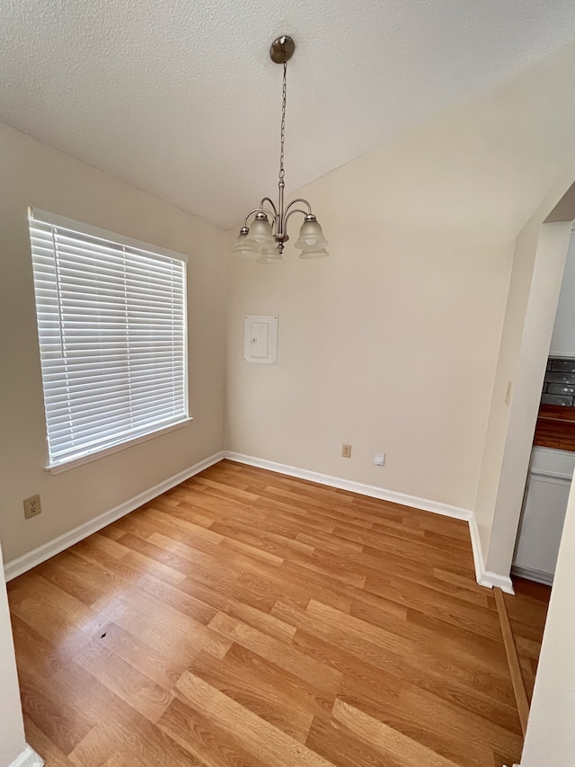 unfurnished dining area with a notable chandelier, a textured ceiling, and light wood-type flooring