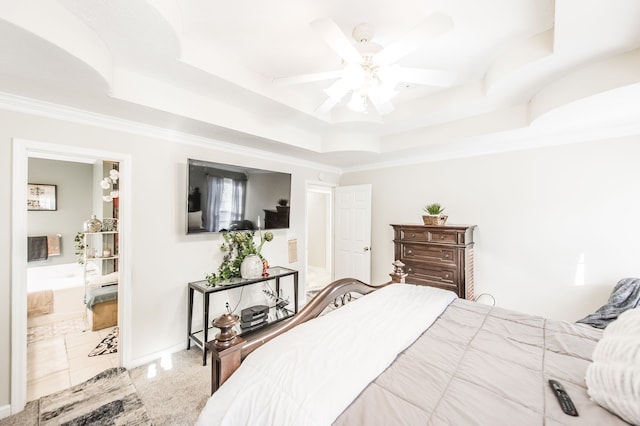 bedroom featuring ceiling fan, ornamental molding, a tray ceiling, and ensuite bath