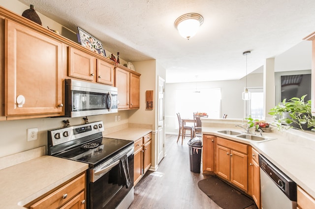 kitchen with hanging light fixtures, sink, appliances with stainless steel finishes, a textured ceiling, and dark hardwood / wood-style flooring