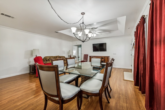 dining room with light hardwood / wood-style floors, ornamental molding, ceiling fan with notable chandelier, and a raised ceiling