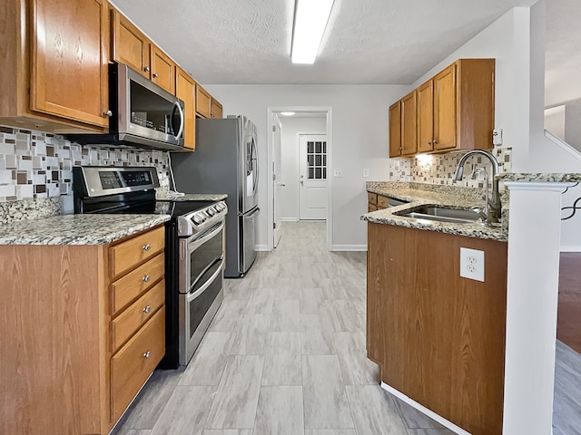 kitchen with stainless steel appliances, backsplash, sink, light stone countertops, and a textured ceiling