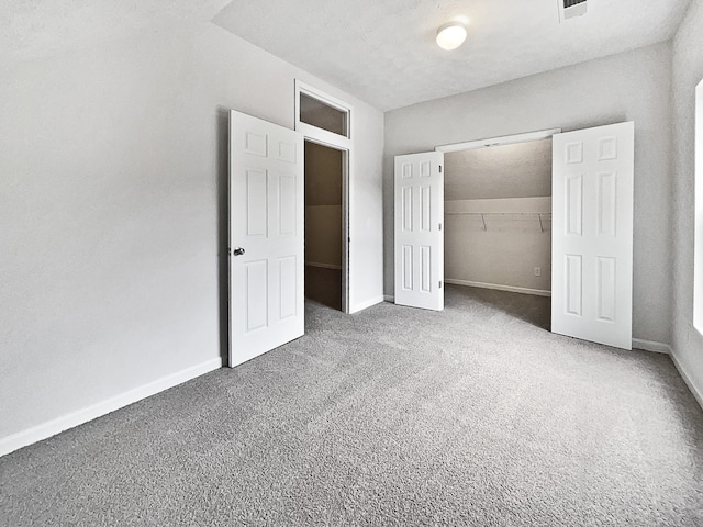 unfurnished bedroom with a closet, a textured ceiling, a spacious closet, and carpet