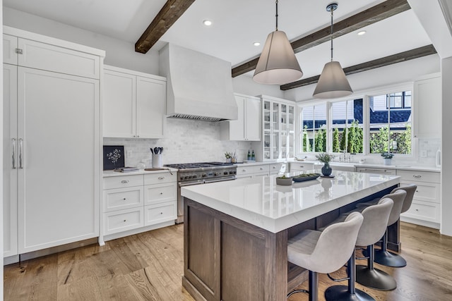 kitchen with beam ceiling, custom exhaust hood, light hardwood / wood-style floors, and high end range